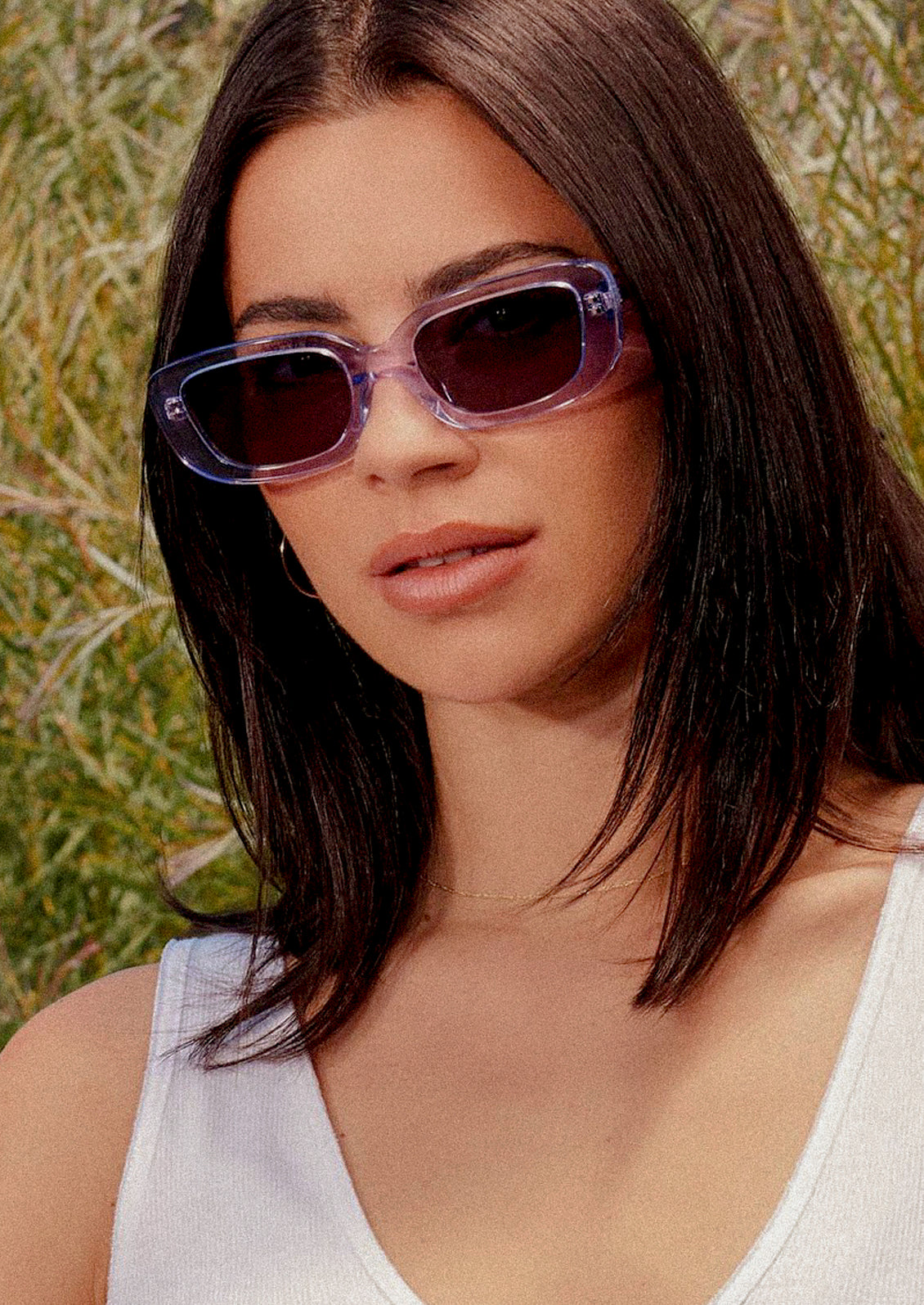 A woman wearing a pair of rectangular sunglasses with clear lilac colored frames.