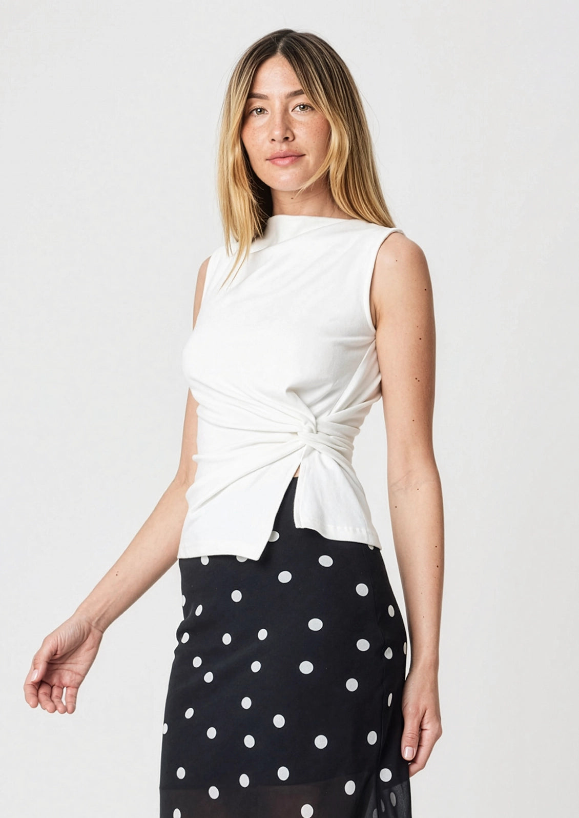 A person wearing a sleeveless white top with asymmetrical twist detail at front.