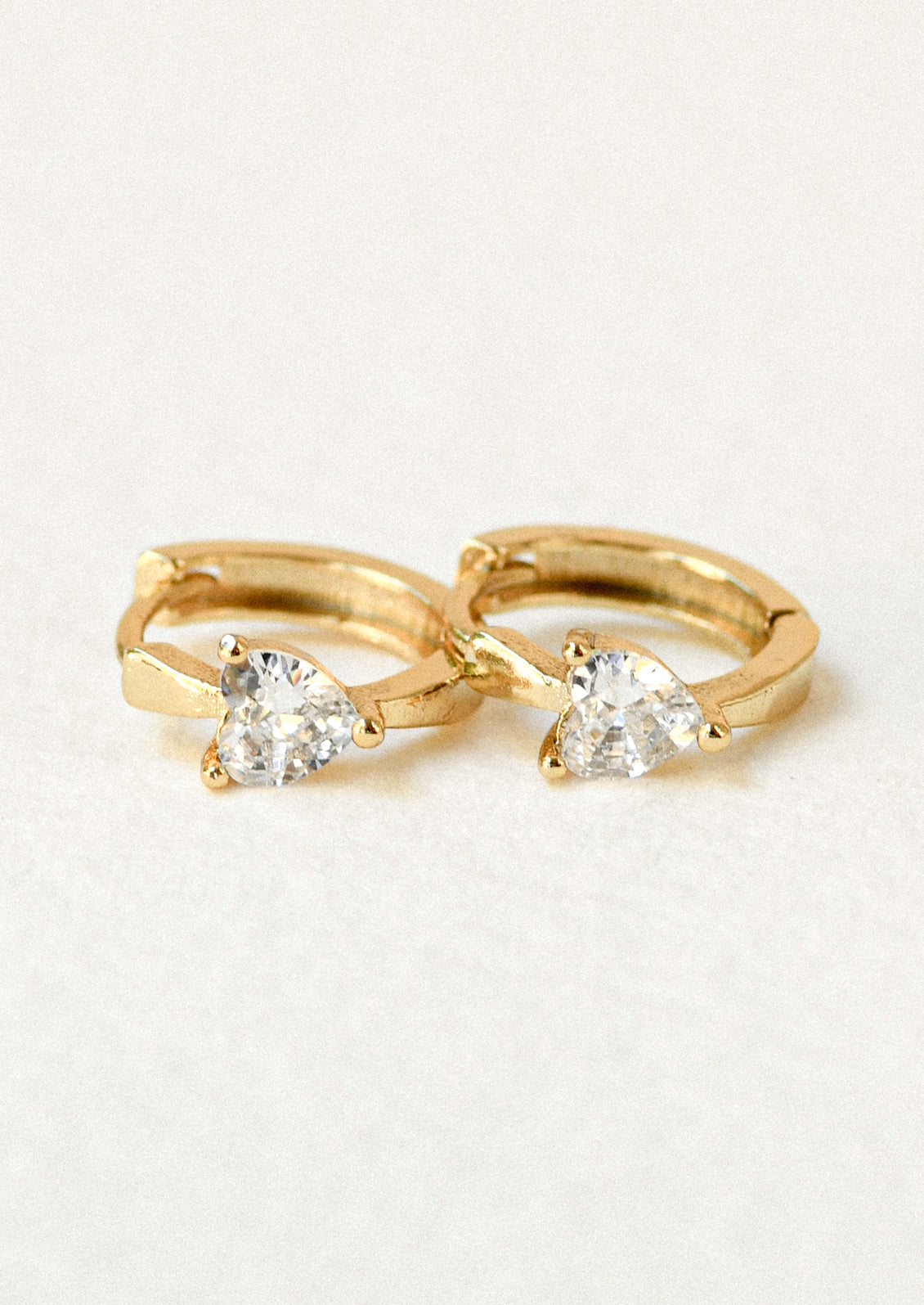 A pair of gold hoop earrings with heart shaped cubic zirconia gems.