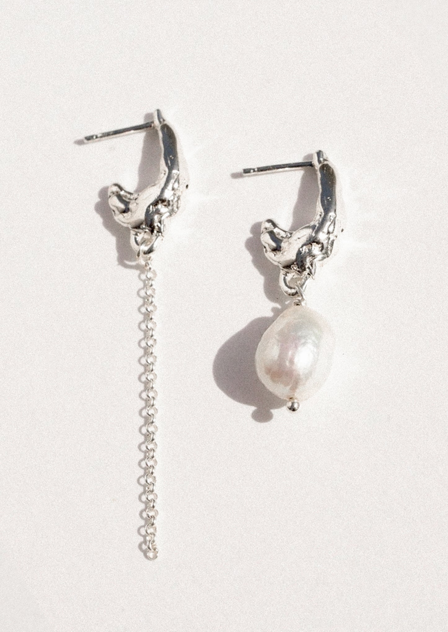A pair of mismatched sterling silver earrings with a freshwater pearl.