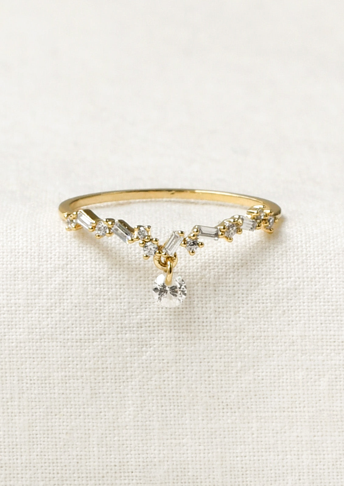 A gold ring with a dipped v design adorned with small variously shaped cubic zirconia and a large round one dangling from the center.