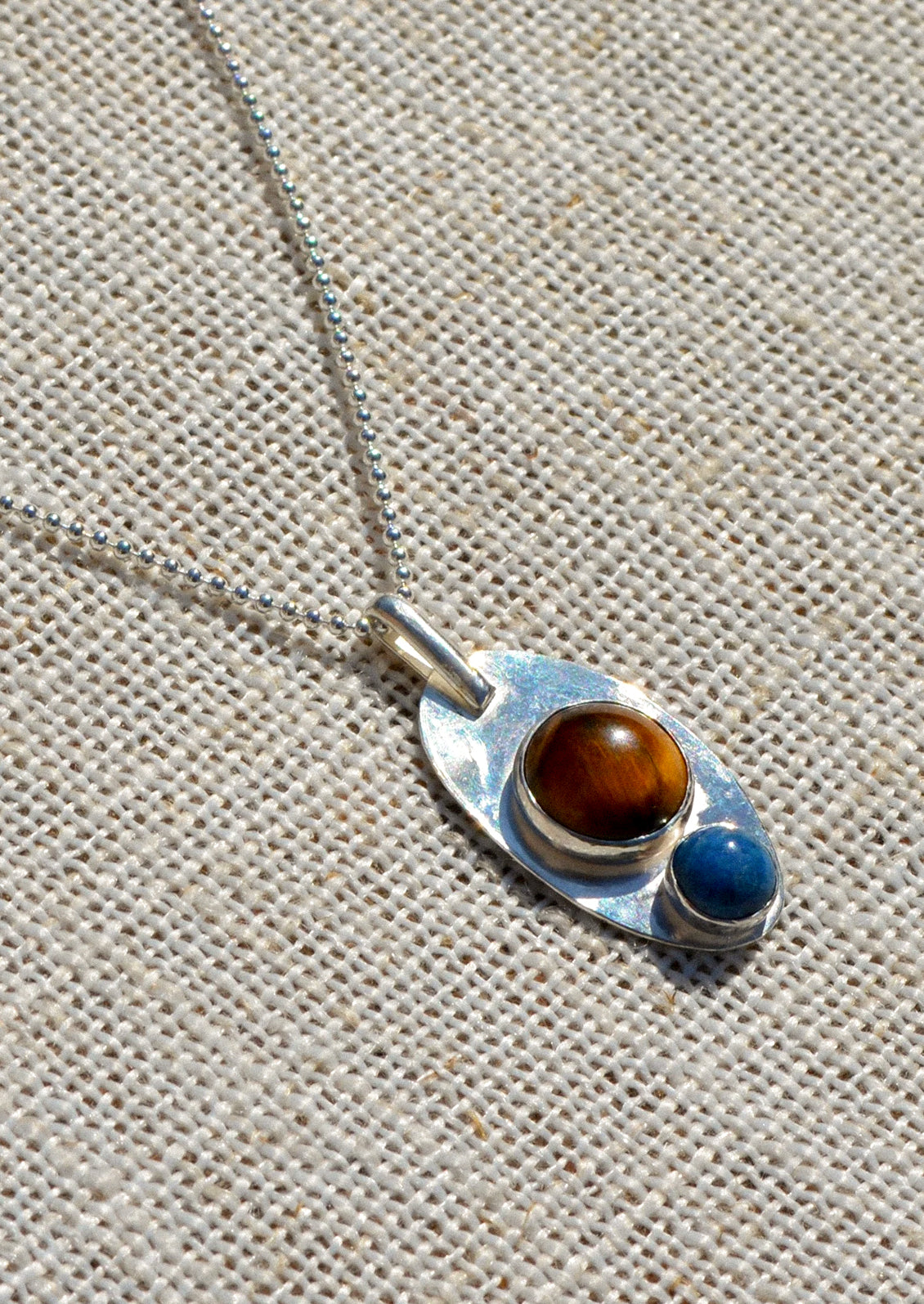 A silver necklace with pendant adorned with a brown gemstone and blue gemstone.