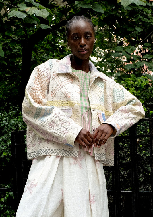 A person wearing a cream jacket with allover pastel embroidery.