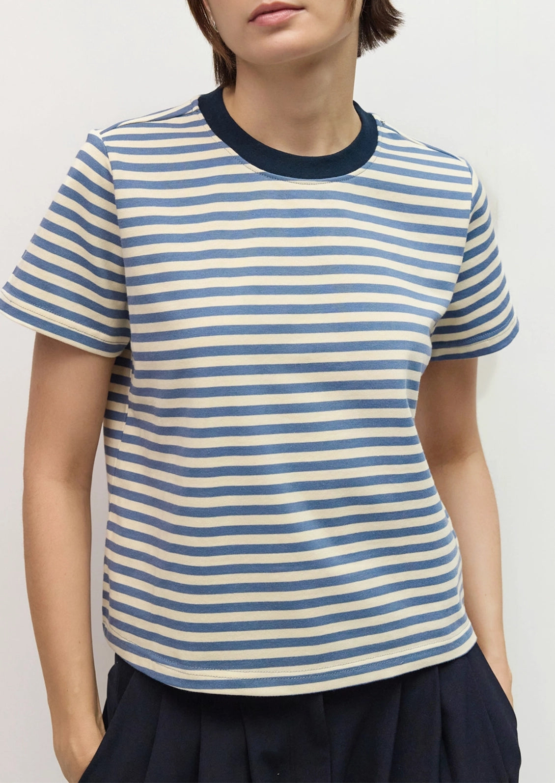 A person wearing a short-sleeve crew-neck striped T-shirt with horizontal navy and off-white stripes.