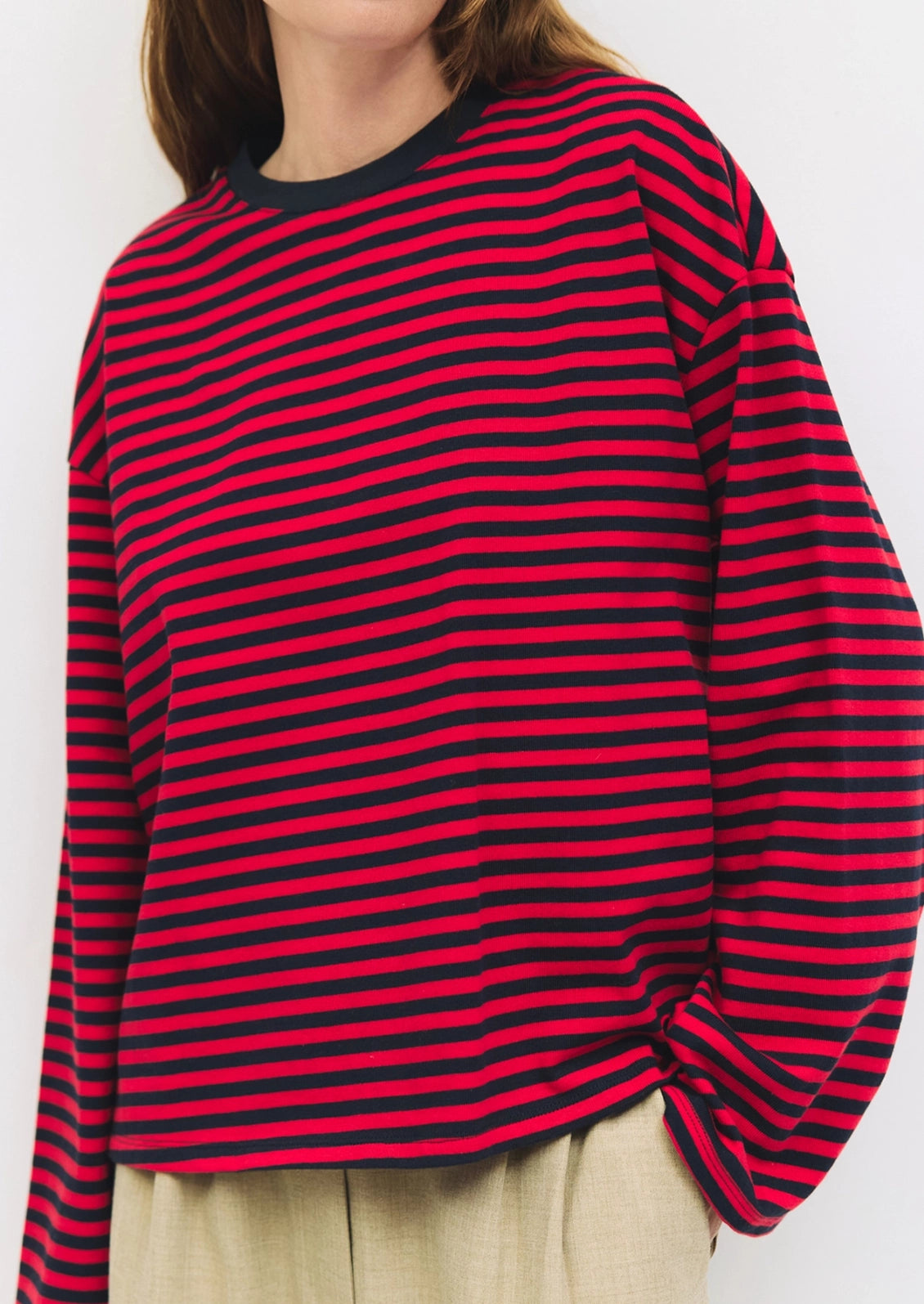 A person wearing an oversized long sleeve tee in red and navy stripes.