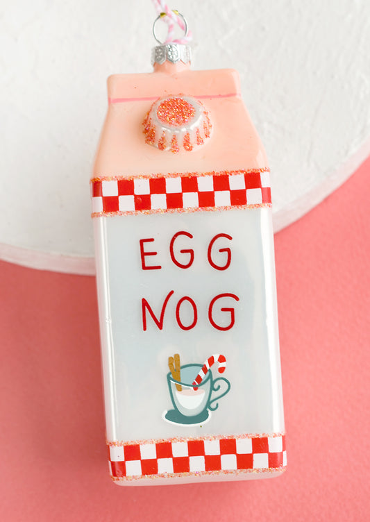 A glass holiday ornament of a carton of egg nog.