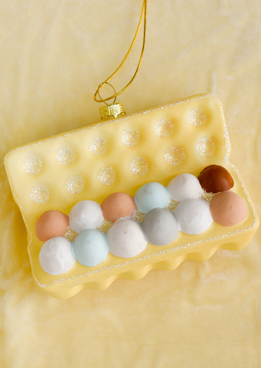 A glass ornament of yellow carton of a dozen multicolored eggs.