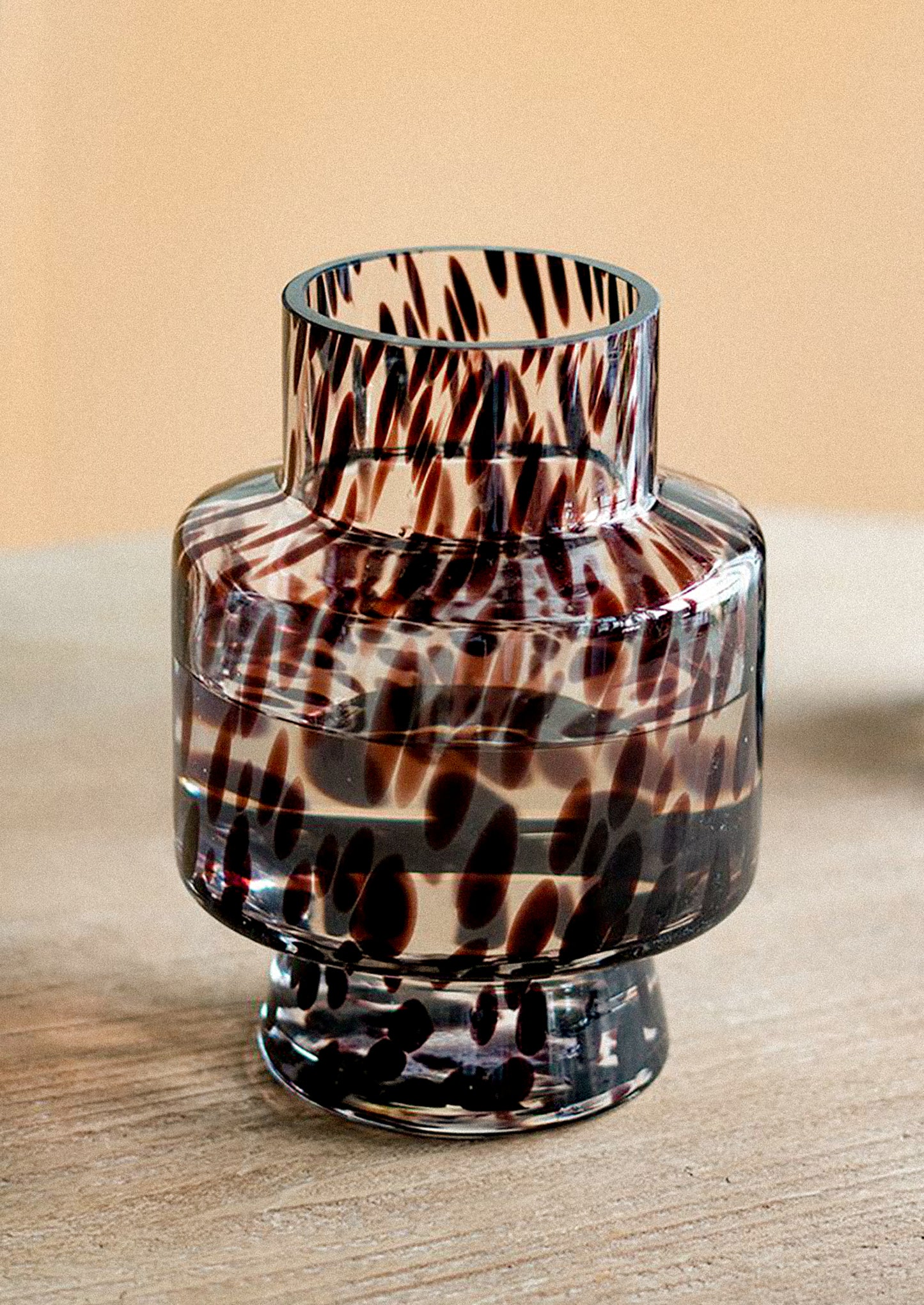 A small clear glass vase with a dark brown and black abstract spotted pattern.