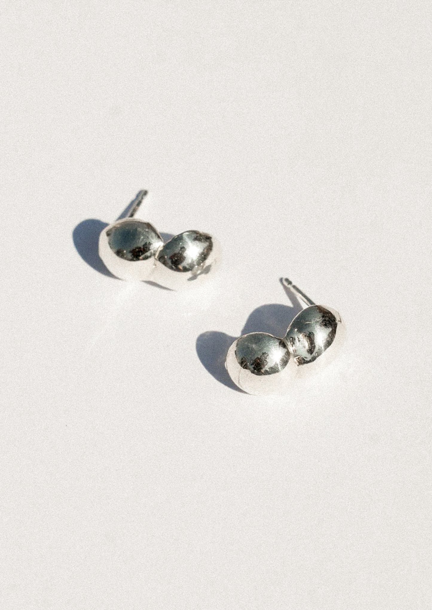 A pair of silver stud earrings with a unique double-oval design, photographed on a clean white background with soft shadows.