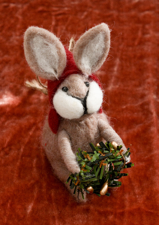 A felted beige bunny ornament wearing red hood and carrying wreath.