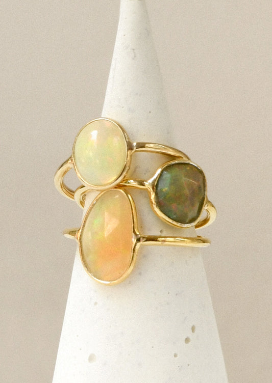 A stack of three gold rings each with a natural Ethiopian opal bezeled in the center in varying sizes and colors.