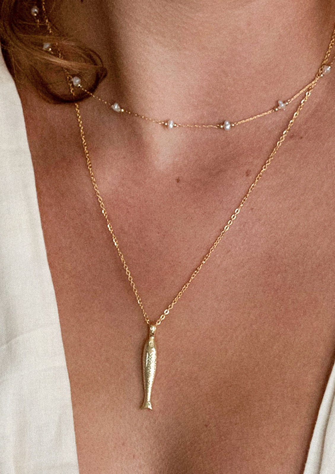 A woman wearing two necklaces, one with a gold fish charm.