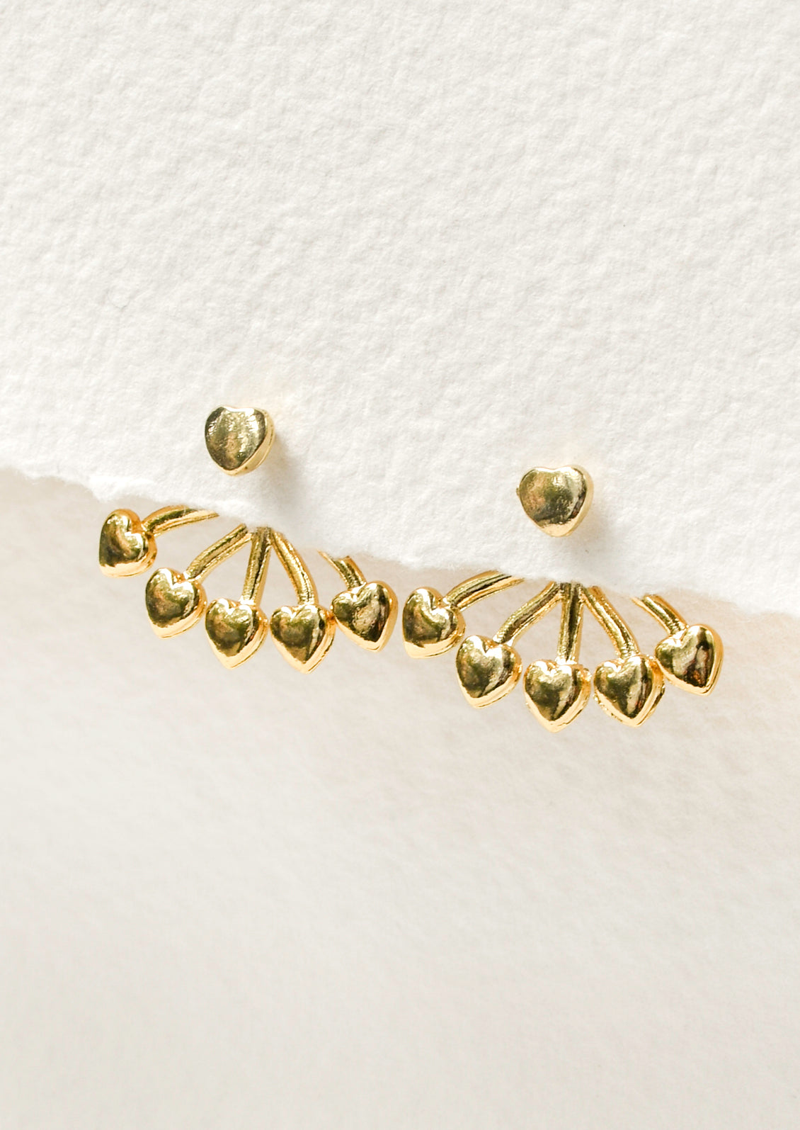 A pair of gold earrings with a heart shaped stud and five small hearts hanging below that attach on the back of the ear. 
