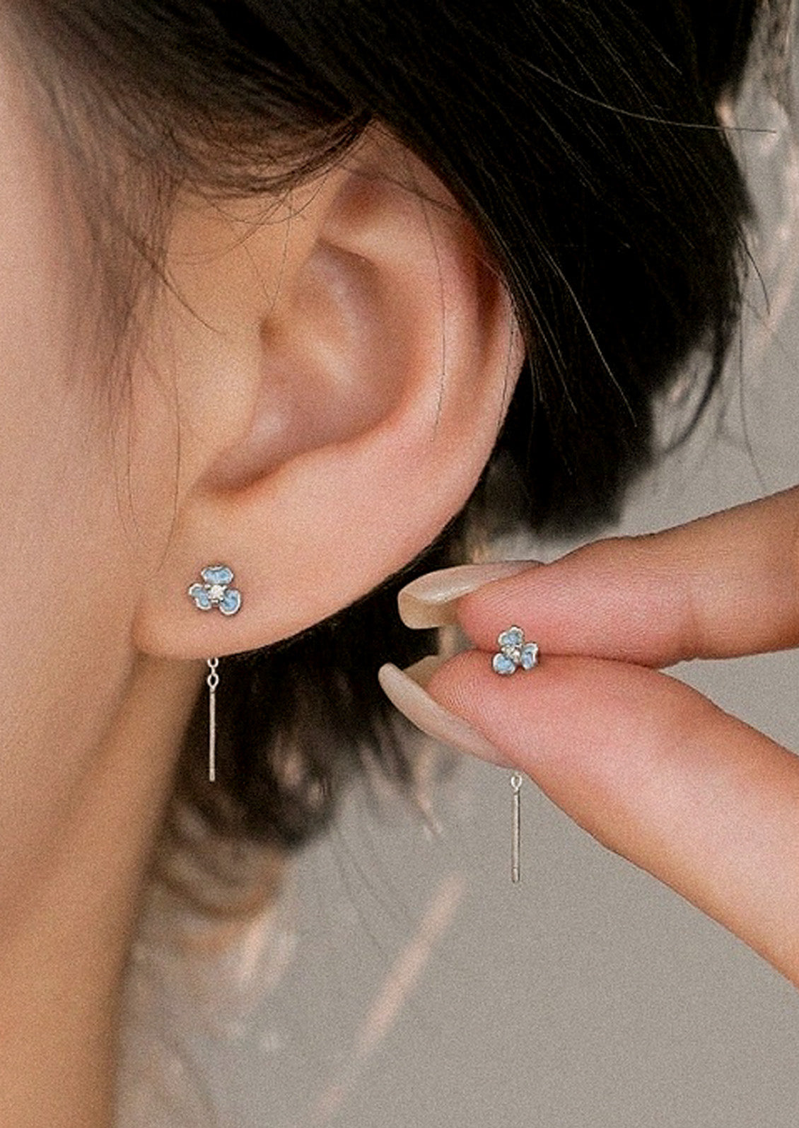A woman wearing a blue flower threader earring in her ear and holding another in between two fingers.