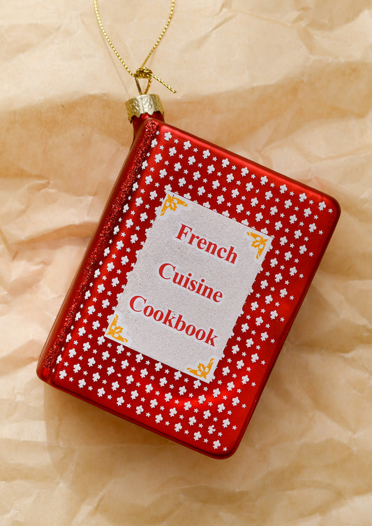 A glass ornament of a red cookbook reading "French Cuisine Cookbook" on cover.