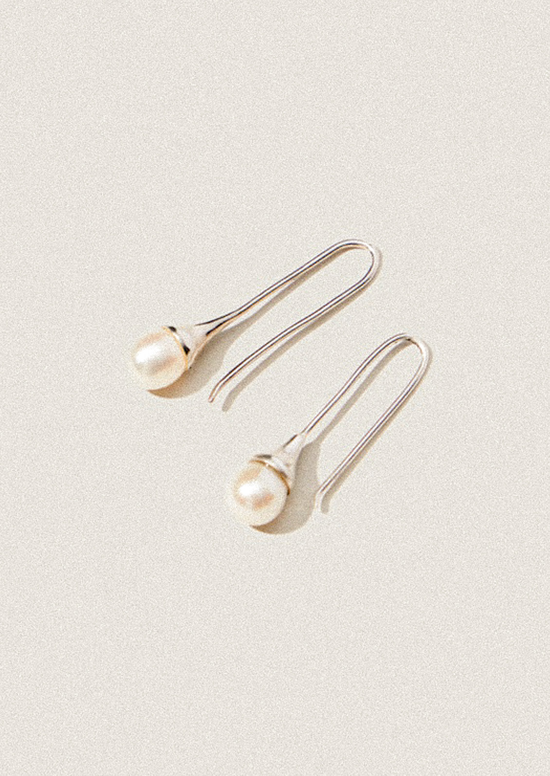 A pair of sterling silver dangling earrings with a freshwater pearl at the end.