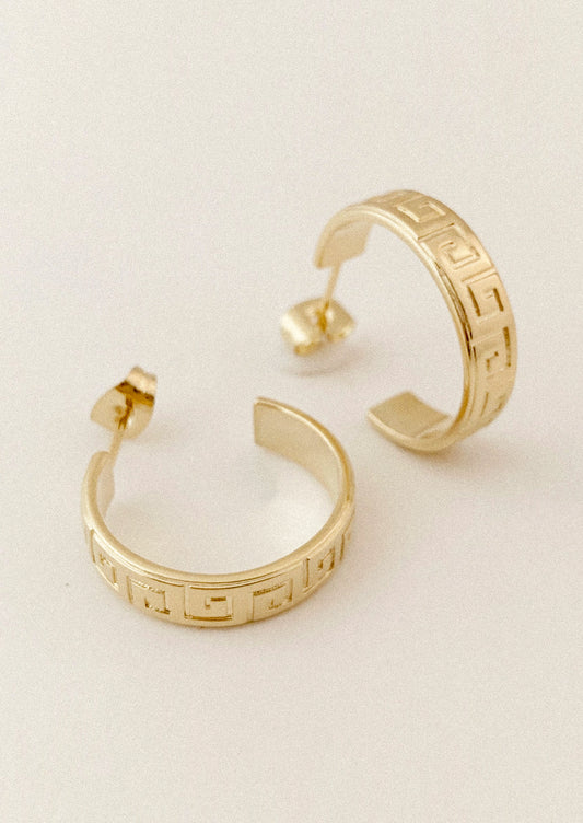 Gold hoop earrings with a Greek key pattern, displayed on a clean off-white background.