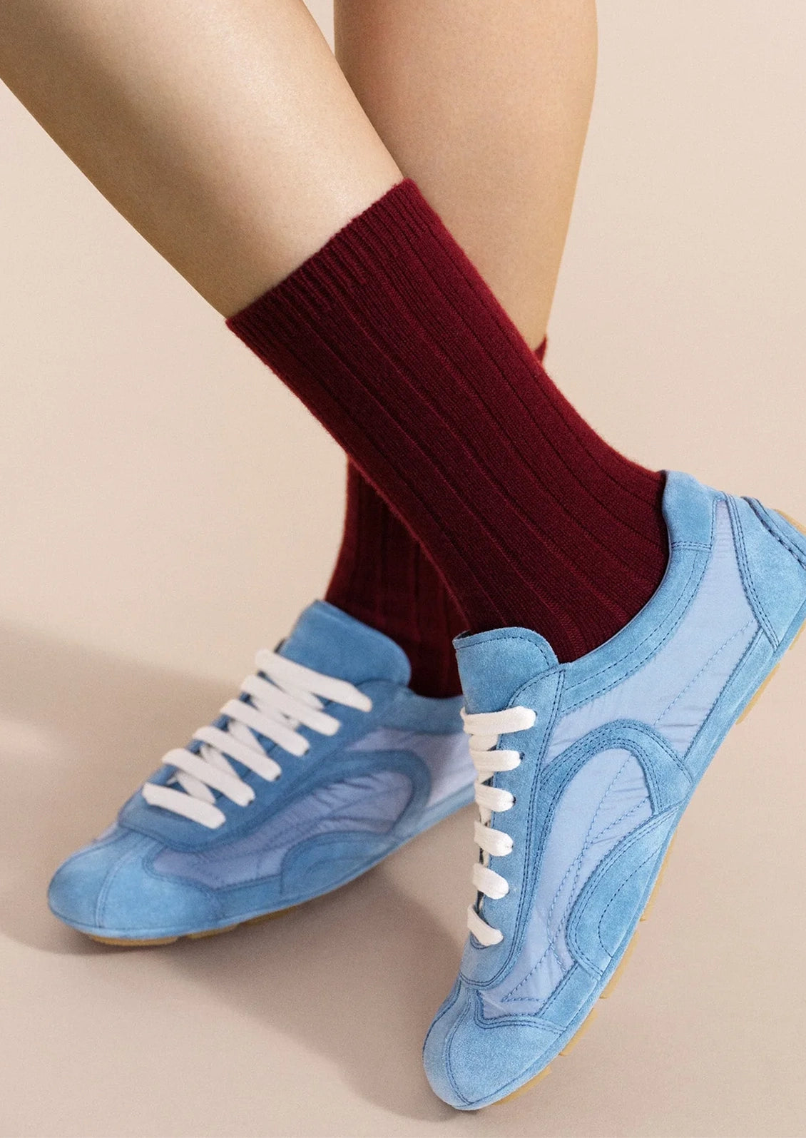 A person wearing ribbed burgundy cashmere socks with a pair of blue sneakers.