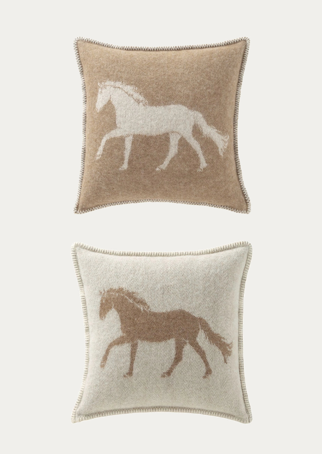 Two square decorative throw pillows with tufted edges, shown against a light gray background. The top pillow is beige with a white horse motif, and the bottom pillow is off-white with a brown horse motif.