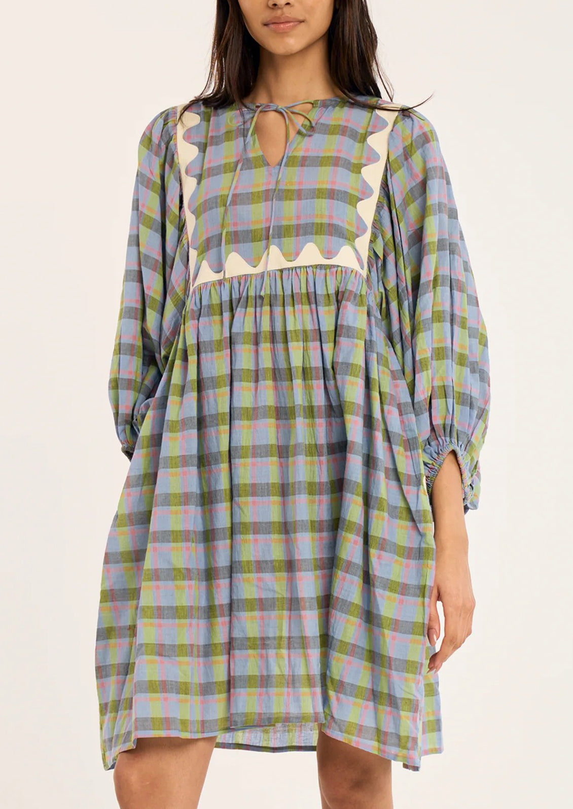 A woman wearing a loose, long-sleeve plaid dress with a keyhole neckline and cream scalloped trim.