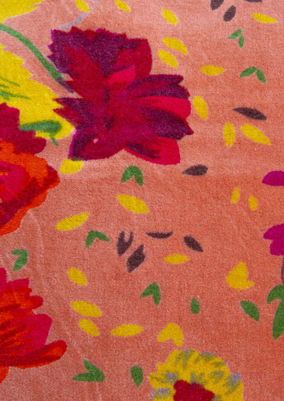 A close-up of a velvet pillow featuring a coral pink background with a bold floral pattern in red, yellow, and green.