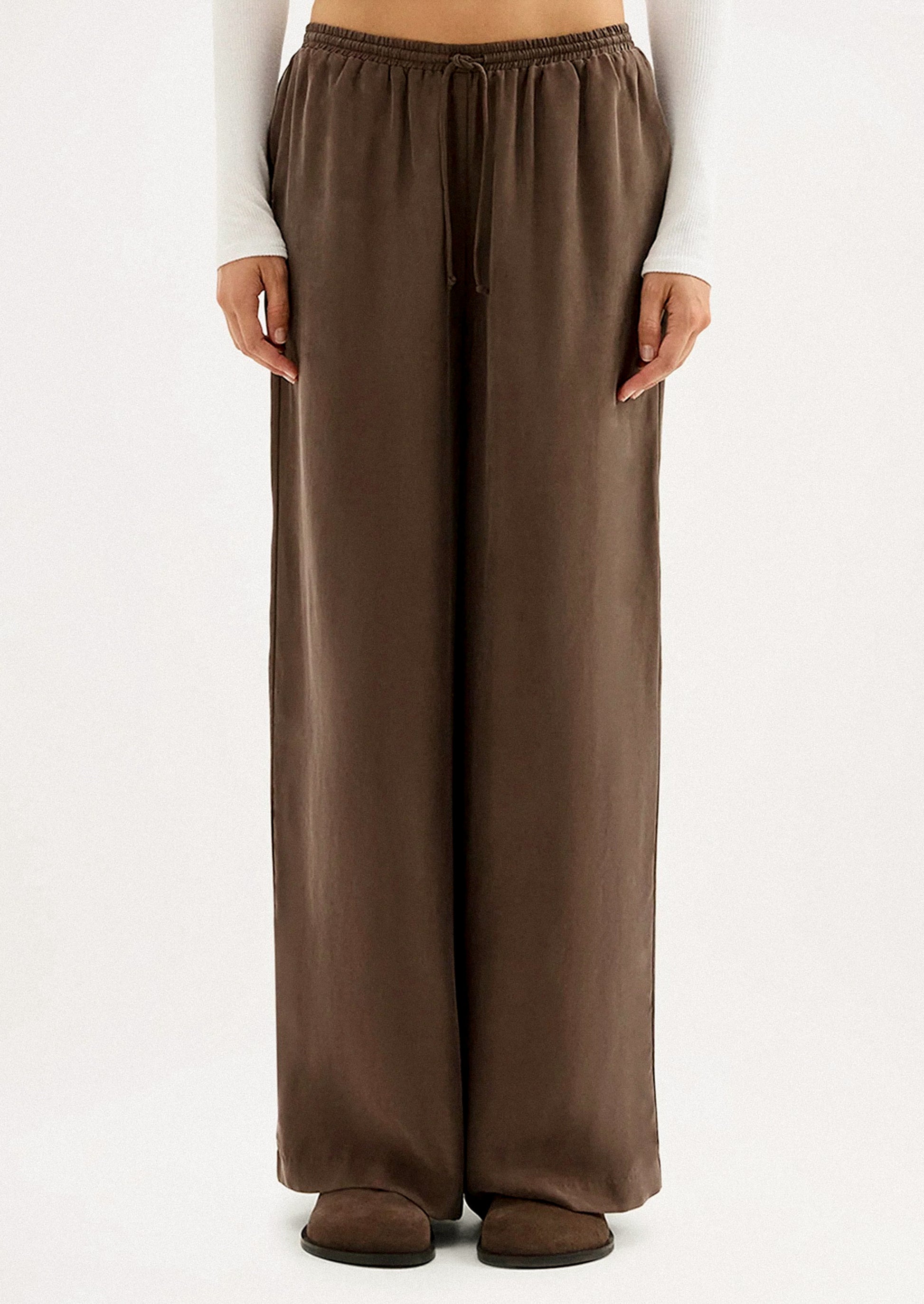 A person wearing a pair of long wide leg pants in brown cupro.