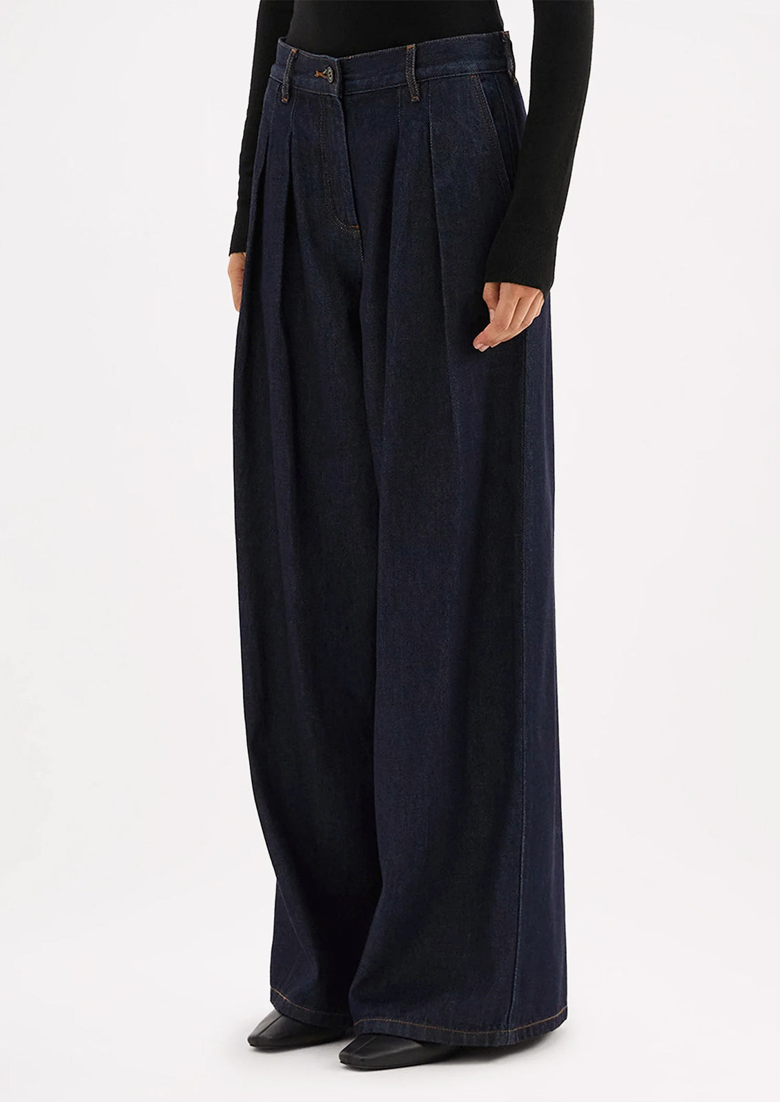 A person wearing a pair of dark rinse wide leg denim trousers with pleated shape.
