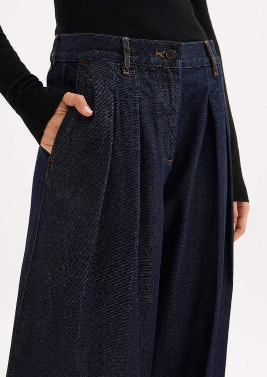 A person wearing a pair of dark rinse wide leg denim trousers with pleated shape.