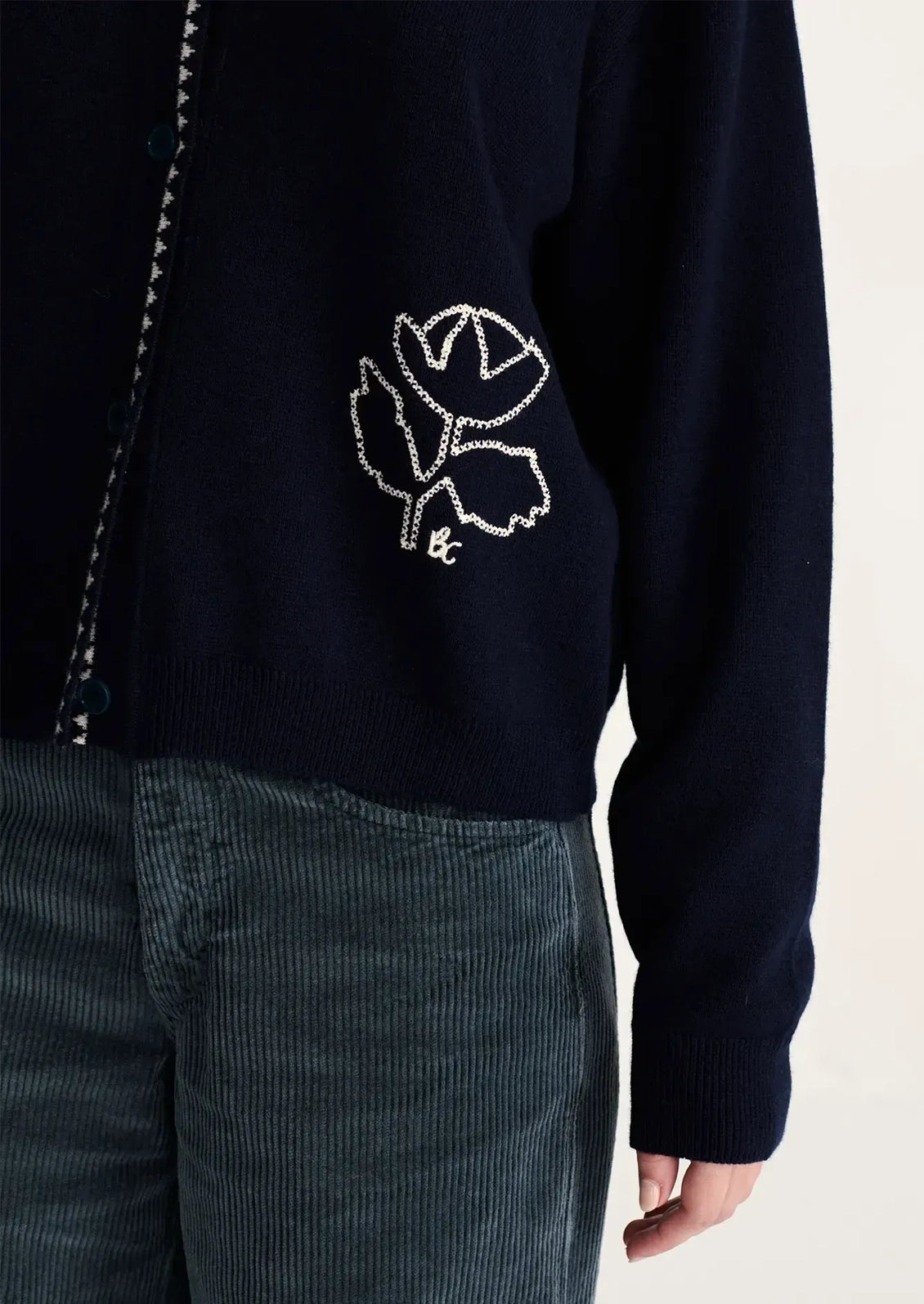 A person wearing a navy blue cardigan with white flower motif at corner.