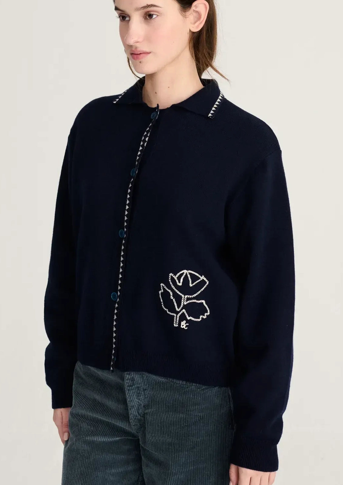 A person wearing a navy blue cardigan with white flower motif at corner.