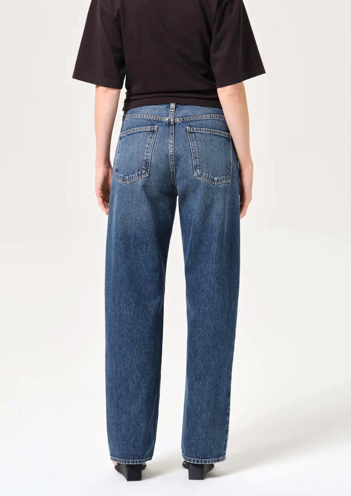 Rear view of a person wearing blue wide-leg jeans and a black short-sleeve top against a plain light background.