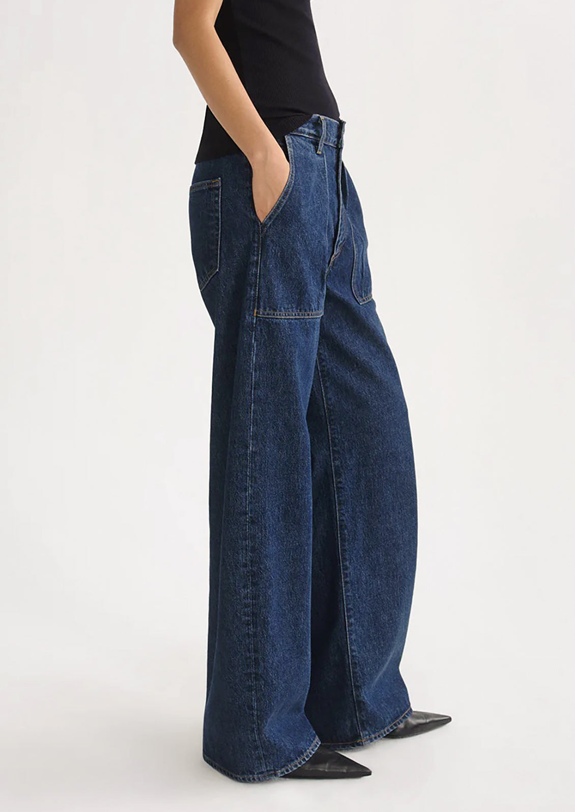 A person wearing a pair of dark denim jeans with pleated pocket front.