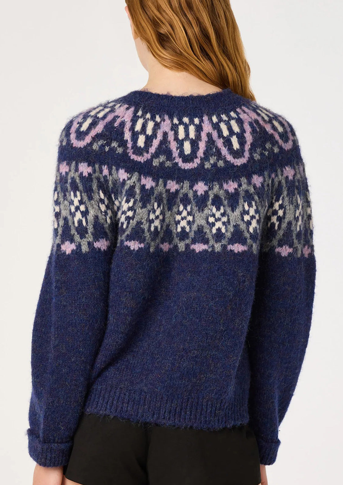 A woman viewed from the back wearing a navy blue fuzzy knit sweater with a light purple, gray, and white Fair Isle pattern across the shoulders and upper back.