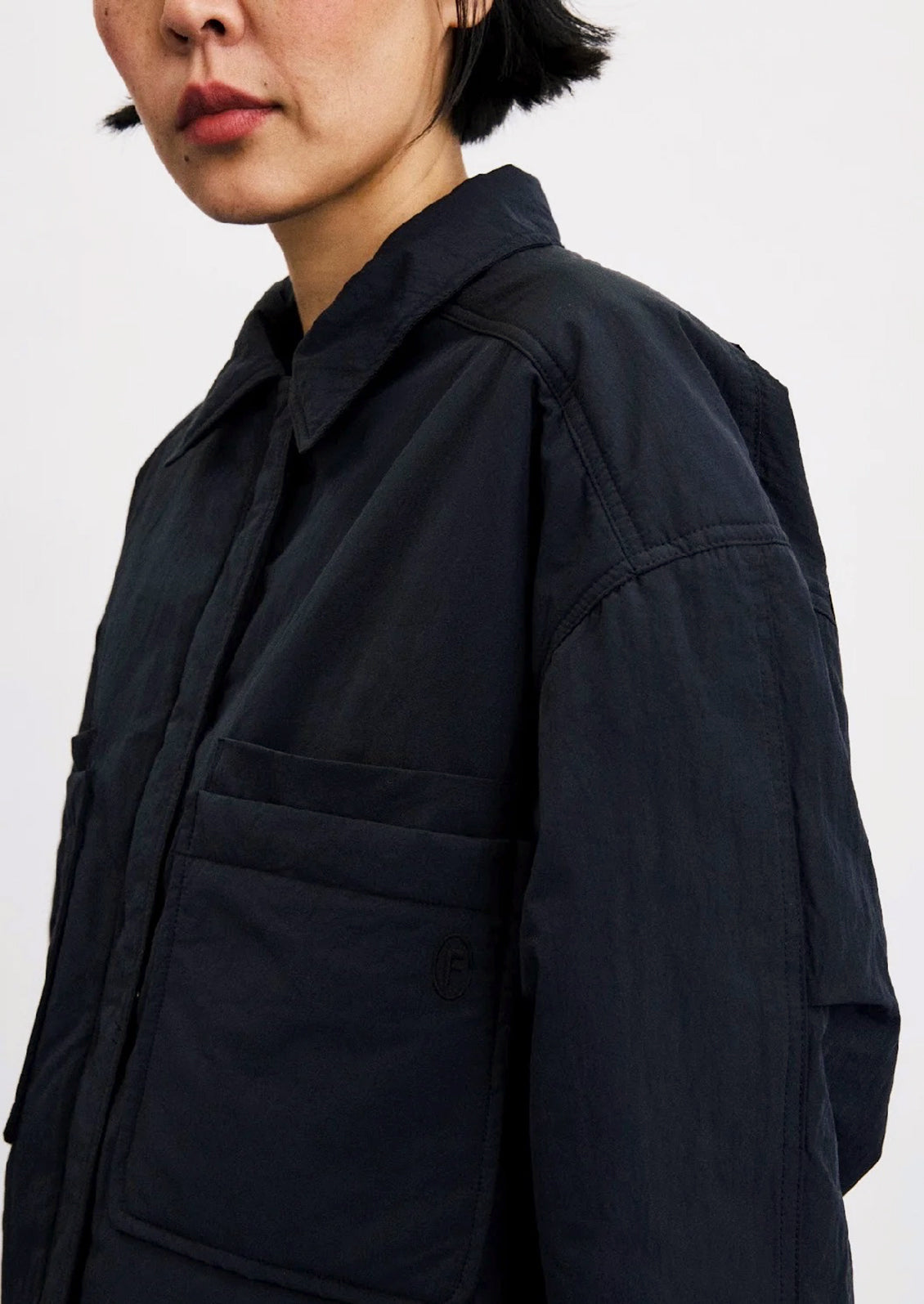 Close-up of a model wearing a dark navy blue utility jacket with a collar, chest pocket, and long sleeves against a plain light background.