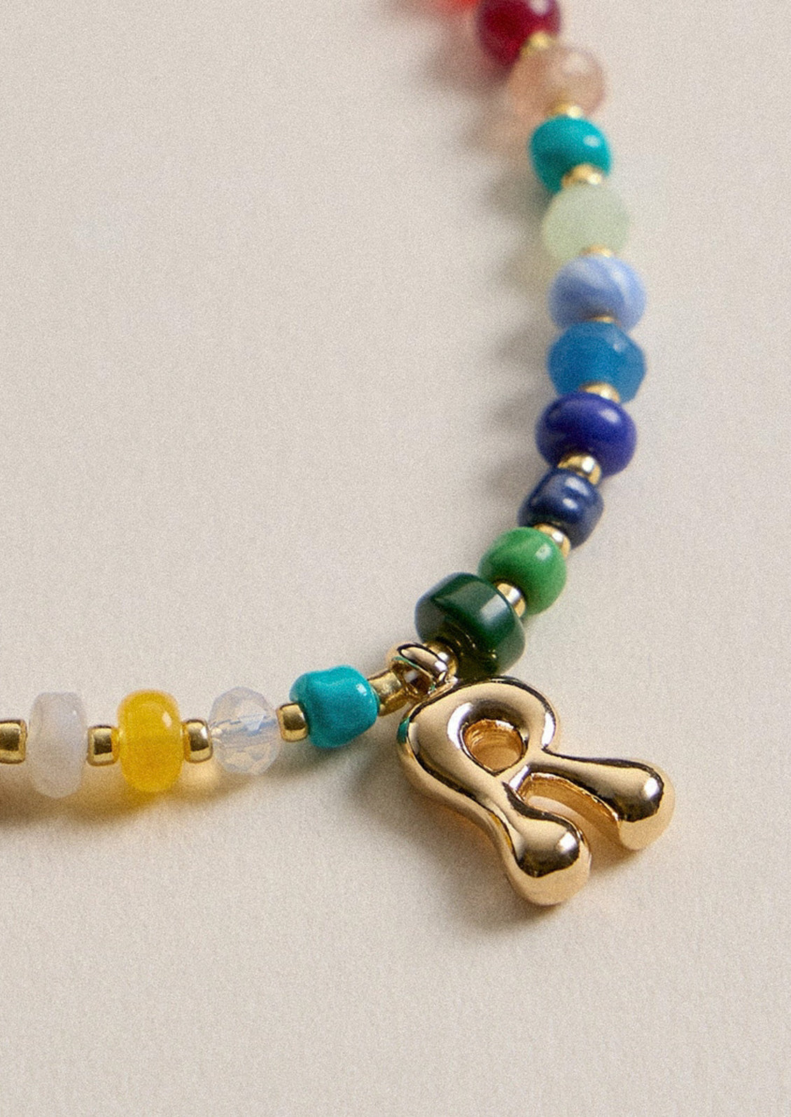 A colorful beaded necklace with a gold R charm.