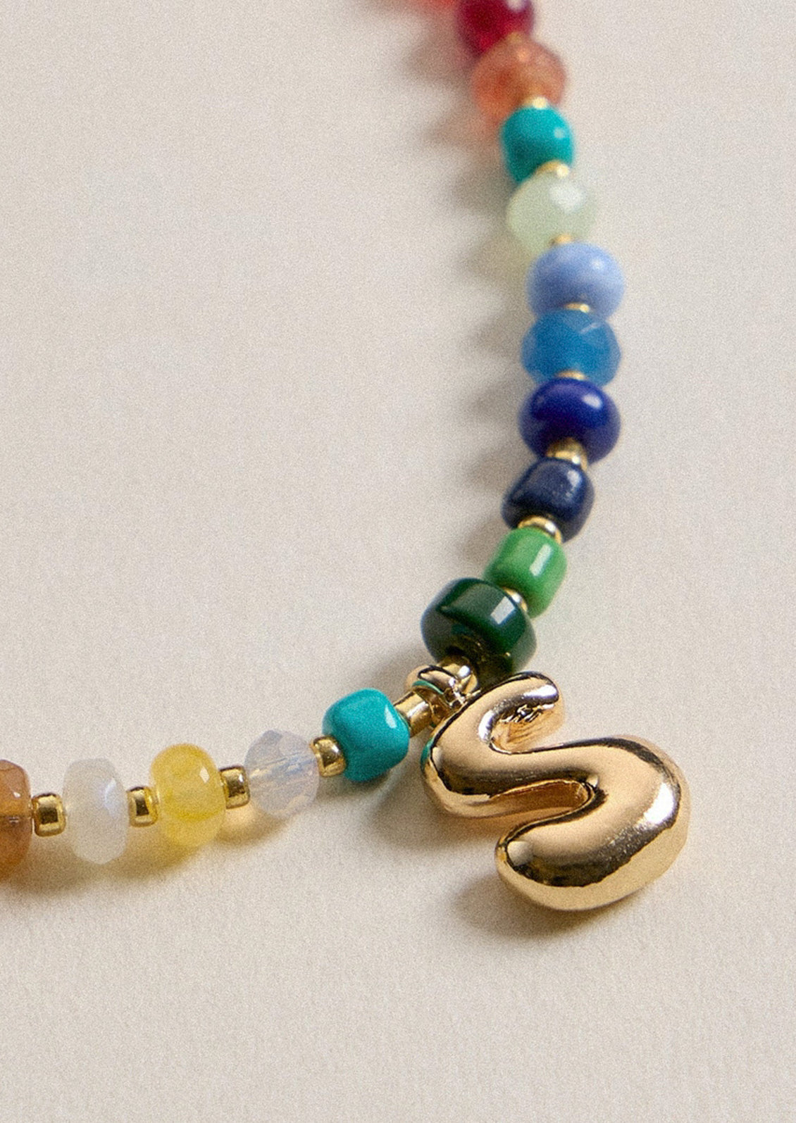 A colorful beaded necklace with a gold S charm.