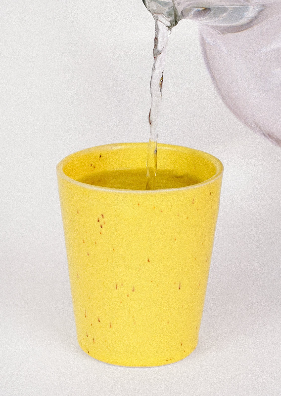 A 12oz ceramic cup in a speckled yellow color with water being poured into it.