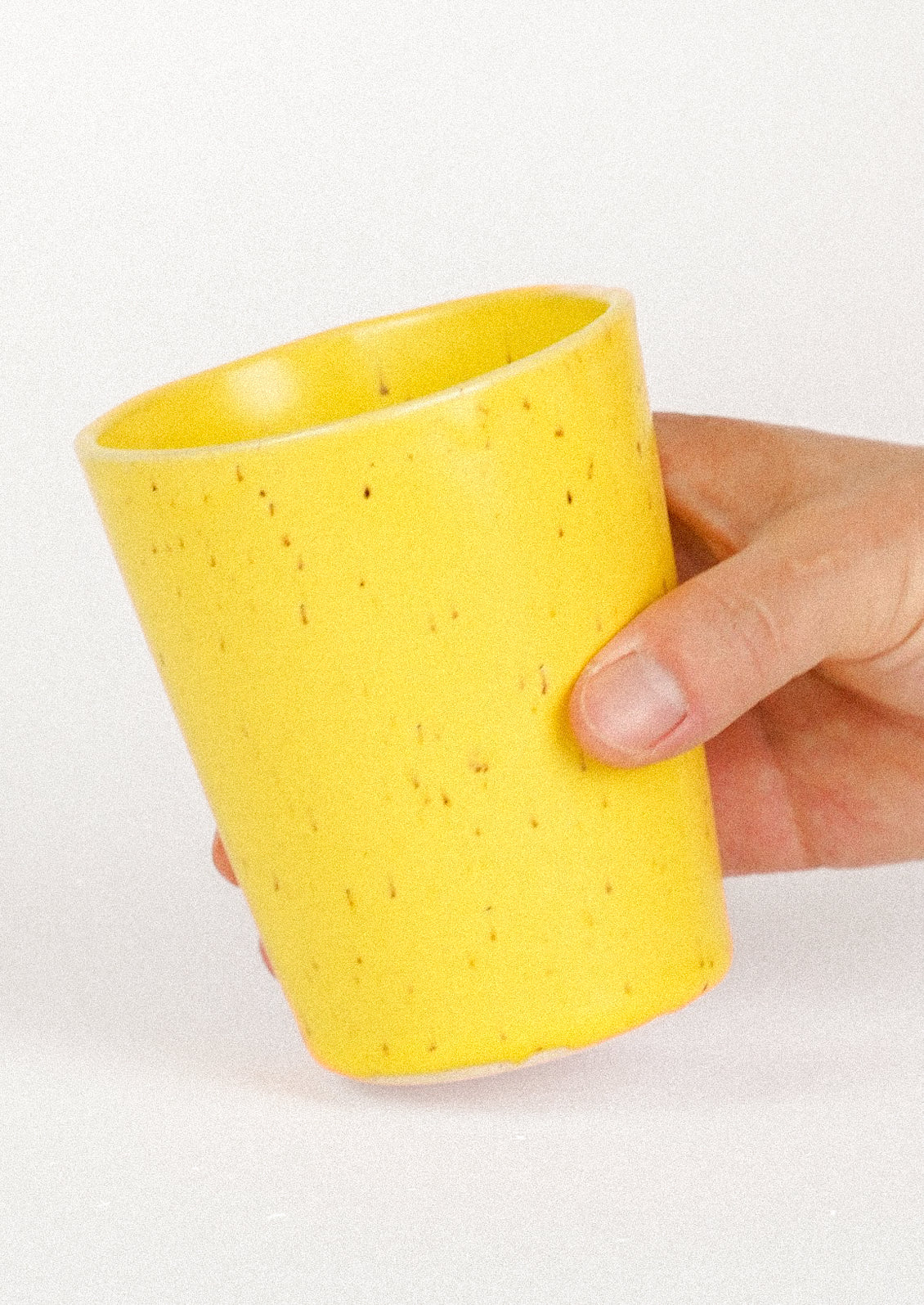A hand holding a 12oz ceramic cup in a speckled yellow color.