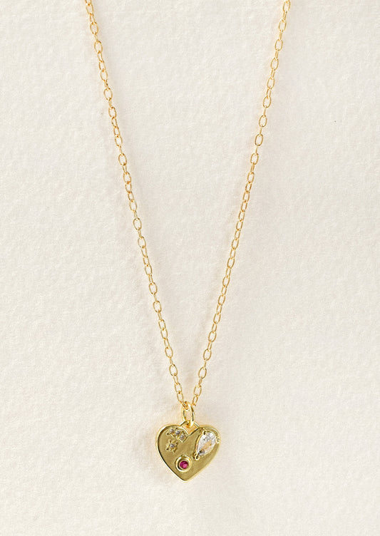 A gold necklace with a gold heart charm adorned with glass crystal and a red gemstone.