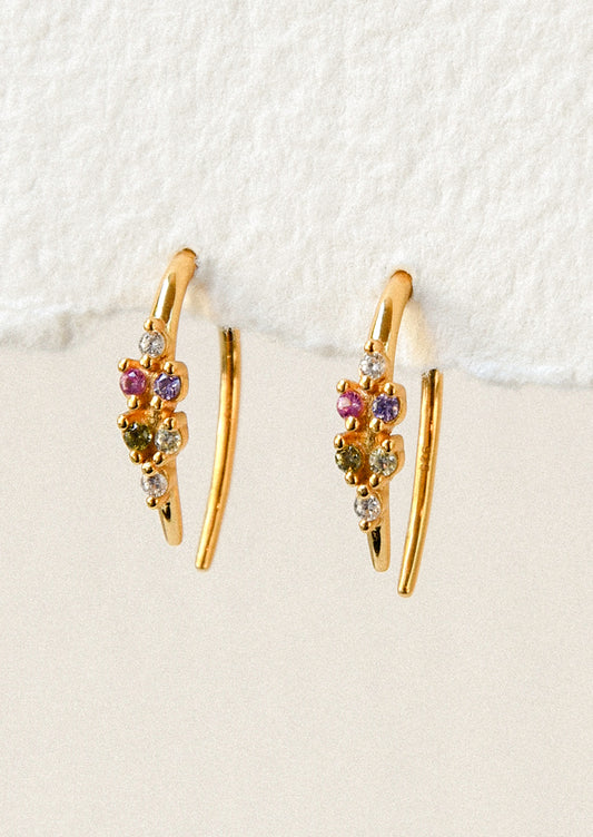 A pair of gold open hoop earrings with various colored glass stones adorned on the front.