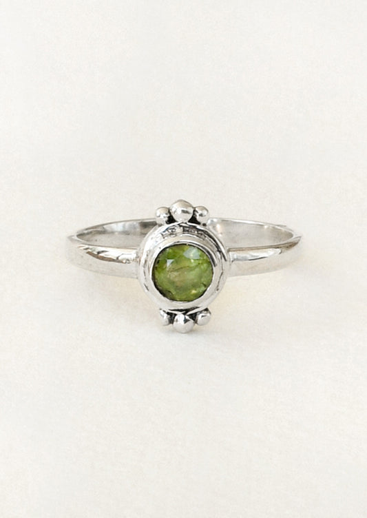 A sterling silver ring with a unique design featuring three tiny spheres on the top and bottom and a peridot gem in the center.