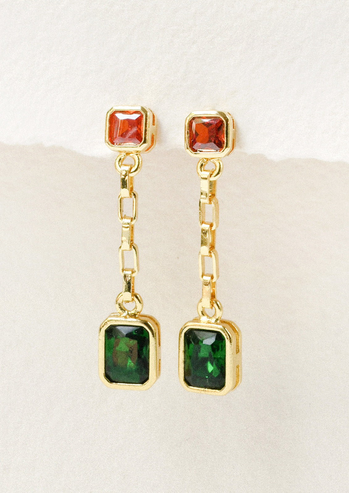 A pair of gold chain dangling earrings with orange and green gems on a white background.
