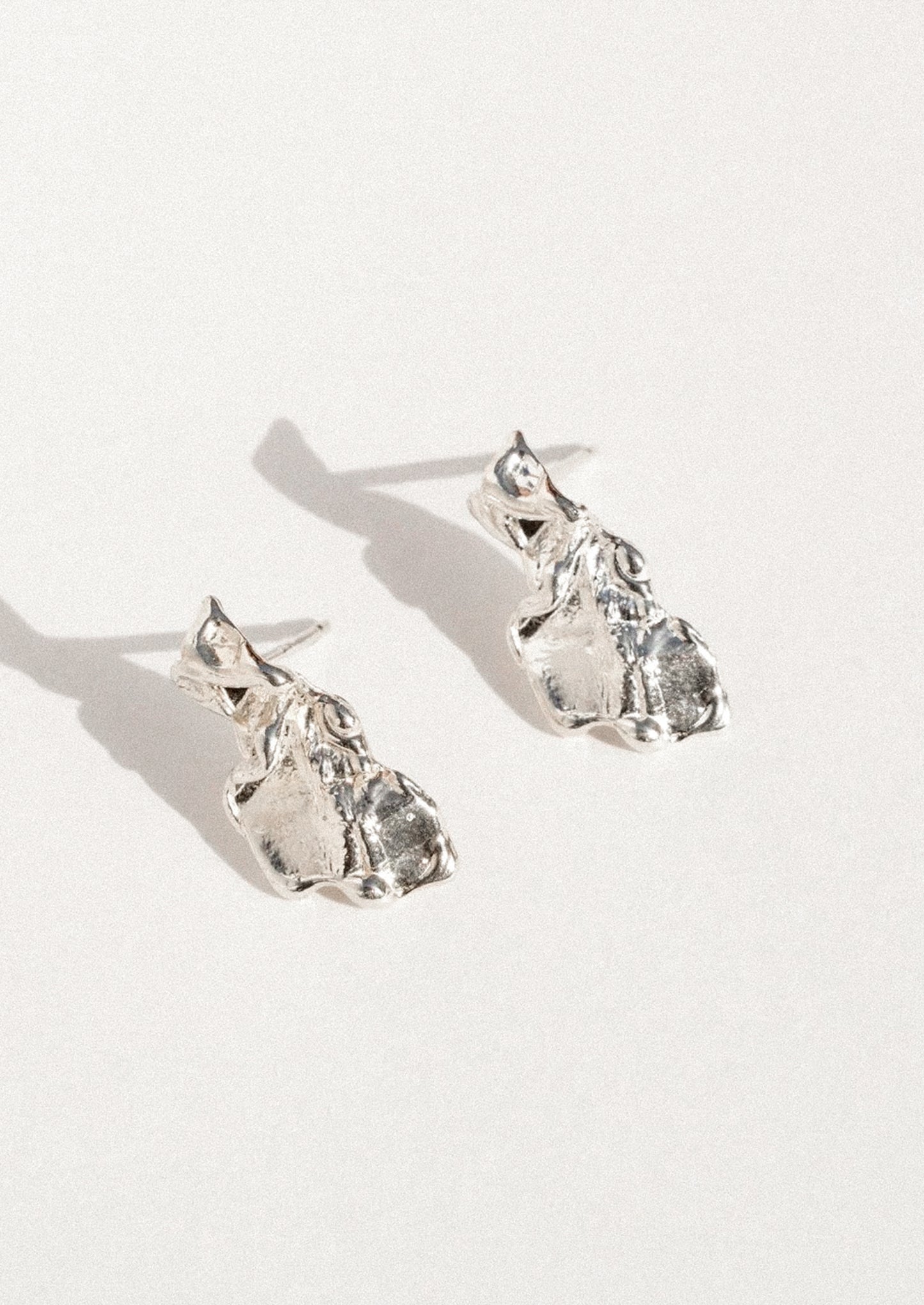 A pair of textured sterling silver stud earrings shaped like small animals, photographed on a clean white background with soft shadows.