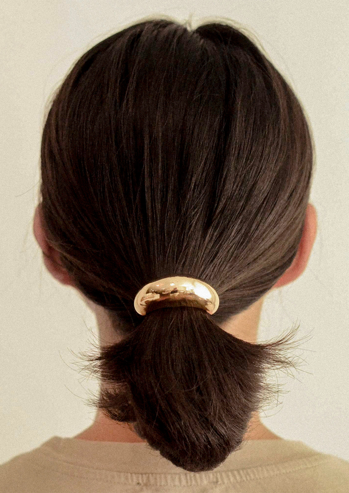 A woman wearing an elastic hair tie with a large gold crescent-shaped metal pendant holding her ponytail.