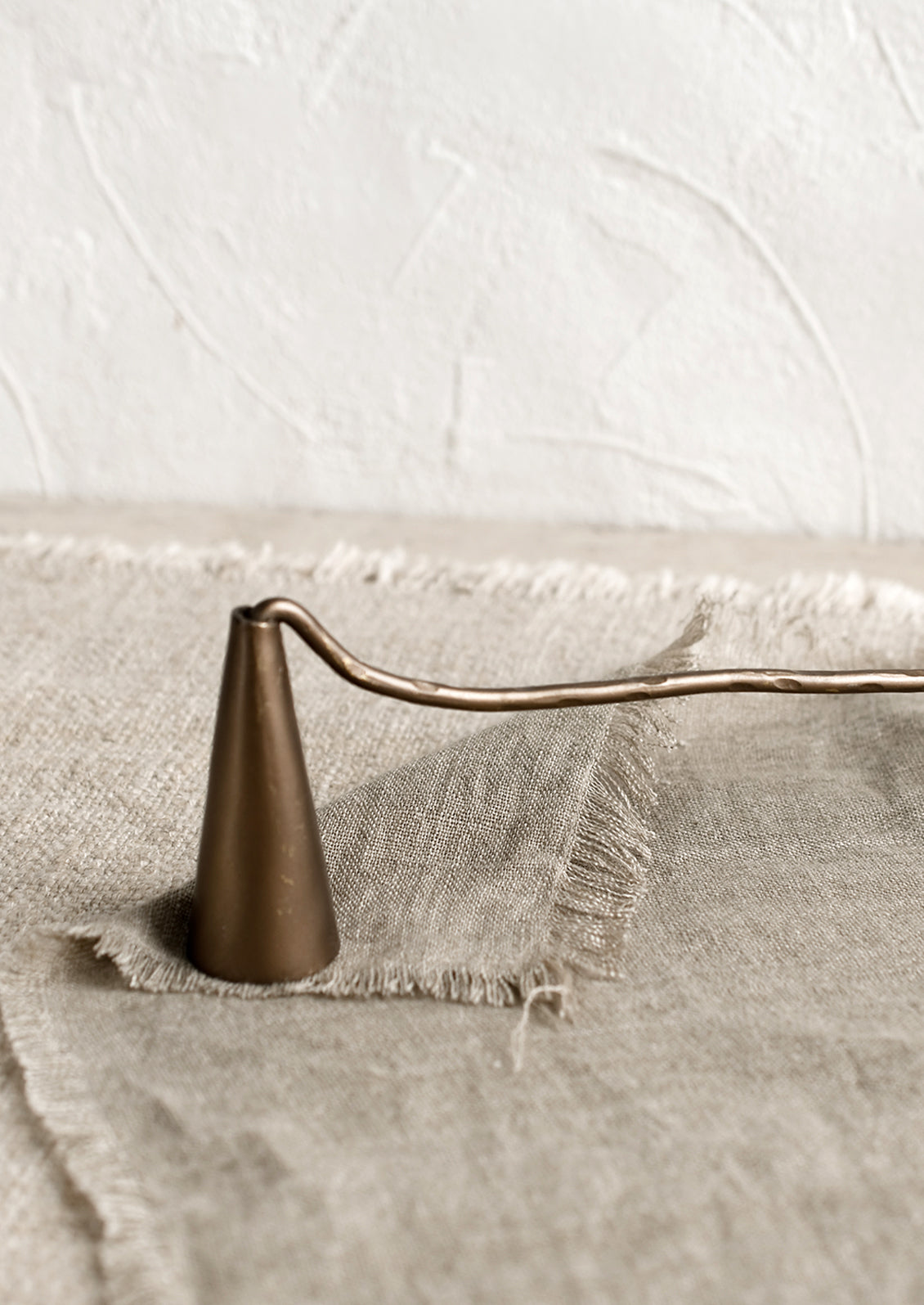 A metal candle wick snuffer with curved handle and tapered shape.
