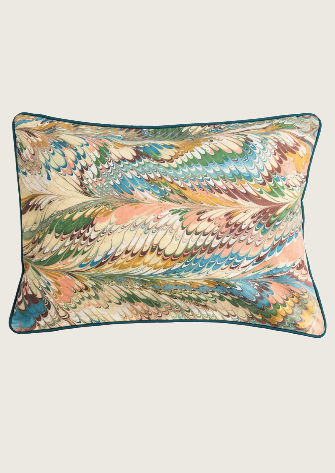 A square decorative throw pillow featuring a vibrant, multicolored feather-like pattern in shades of blue, green, pink, and gold, finished with a dark teal piped edge, shown against a solid light beige background.