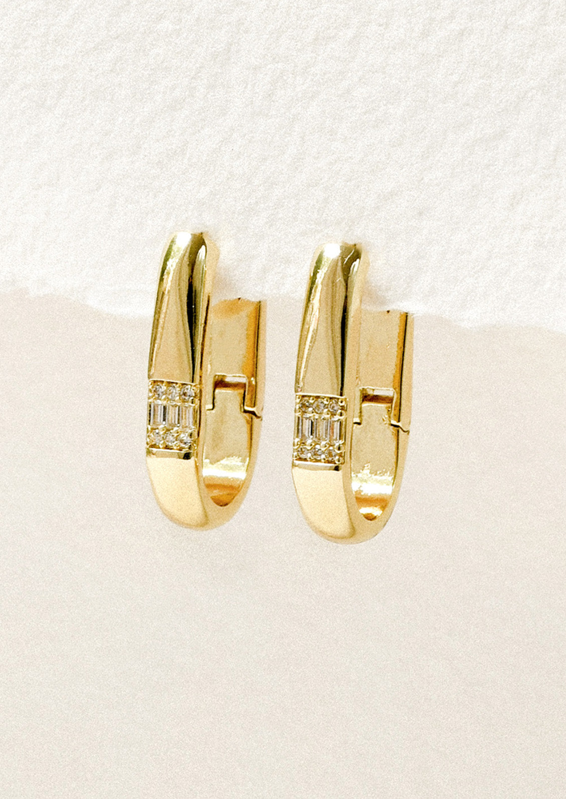 A pair of gold oval hoop earrings adorned with crystals hanging on a white background.