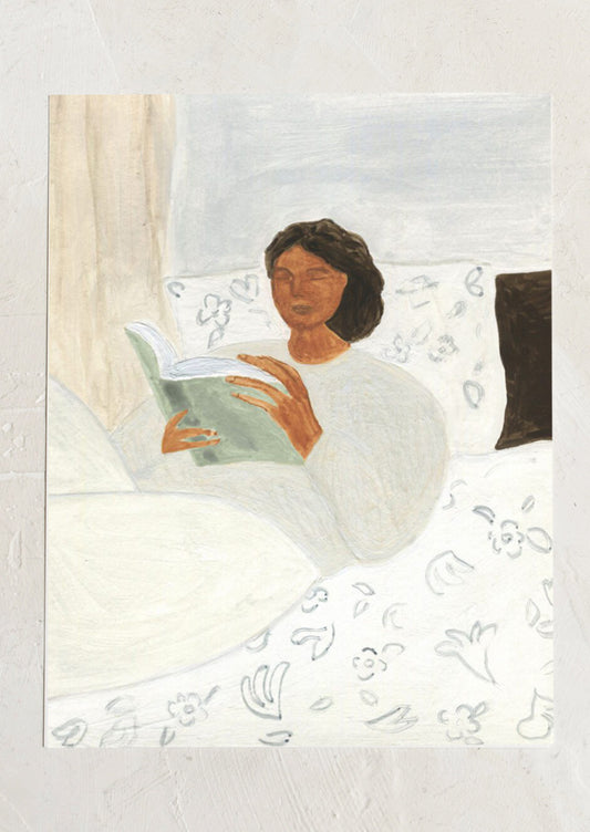 An art print of a painting of a woman laying in bed reading a book.