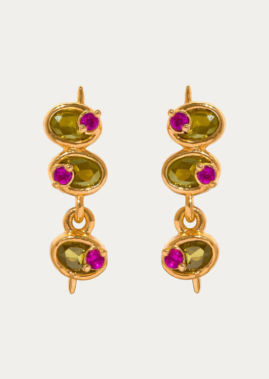 A pair of long gold stud earrings in the shape of olives with green and pink gems on a white background.