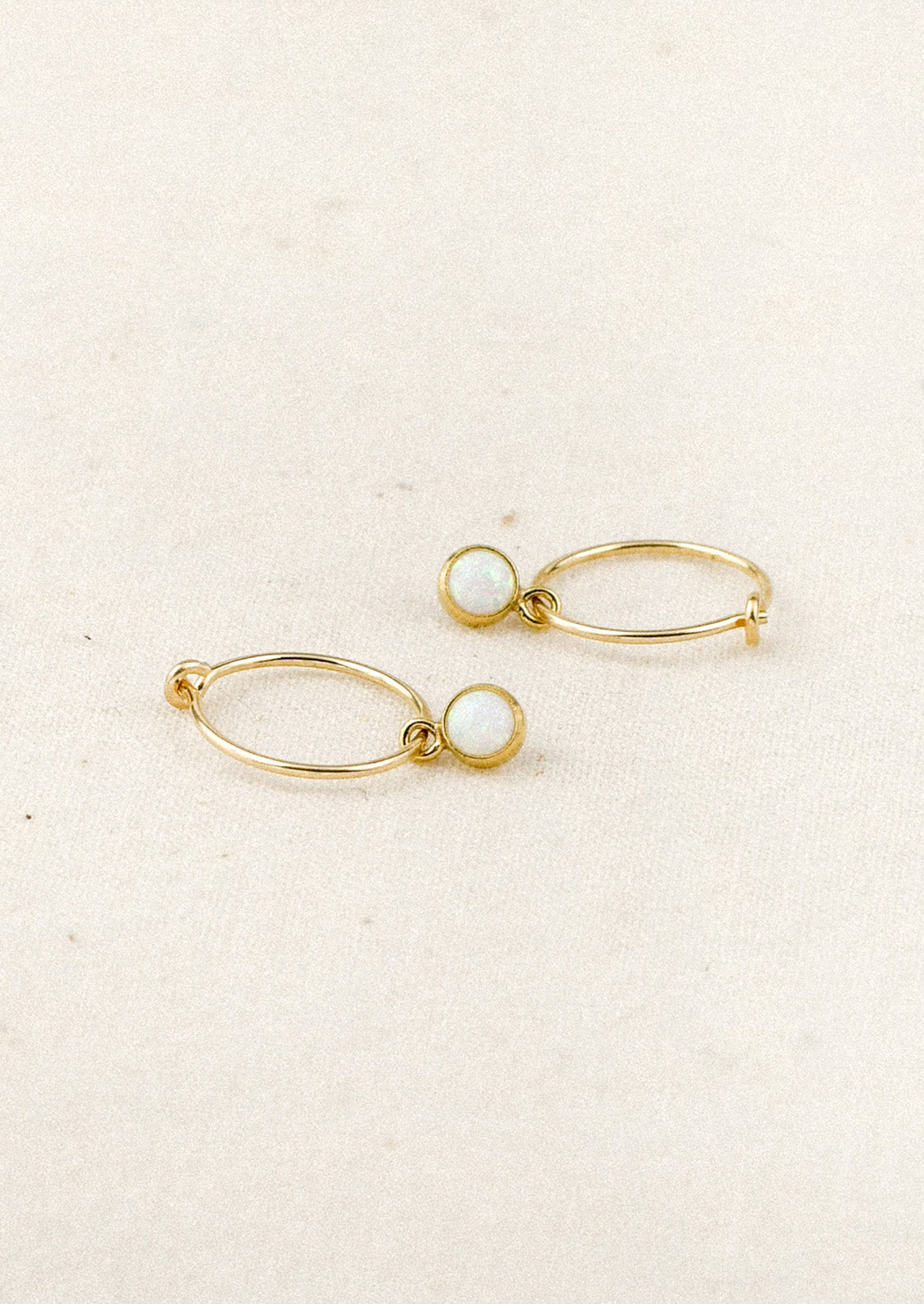 A pair of small gold hoop earrings with bezeled opals.